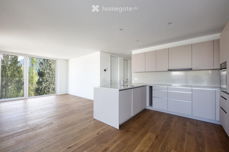 Modern kitchen with light-colored cabinets, a central island, and large windows overlooking greenery.