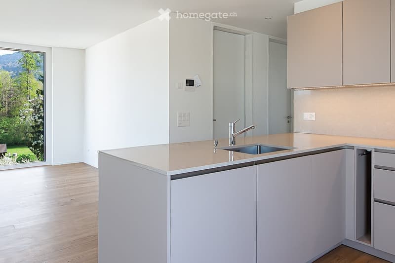 Modern kitchen with light-colored cabinets, a central island, and a sink, featuring a scenic view through a large window.