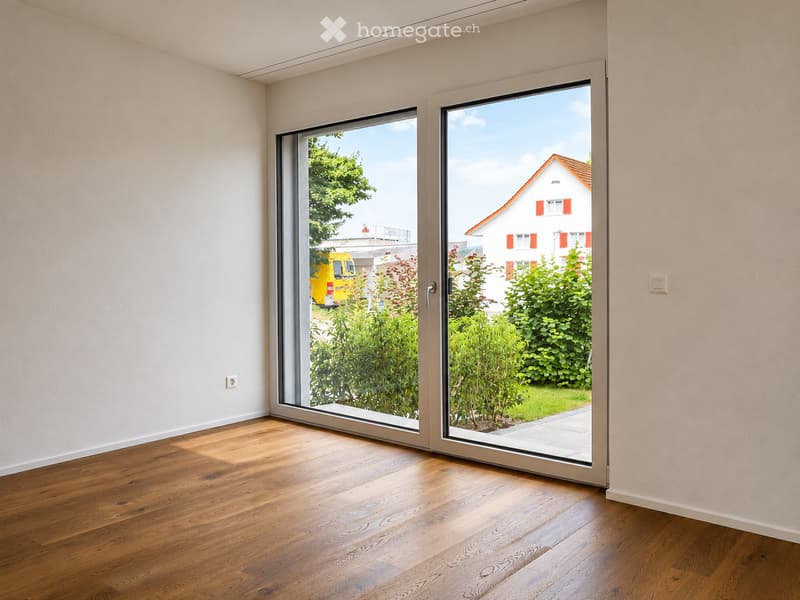 Empty room with wooden flooring and large sliding glass doors leading to a garden area.