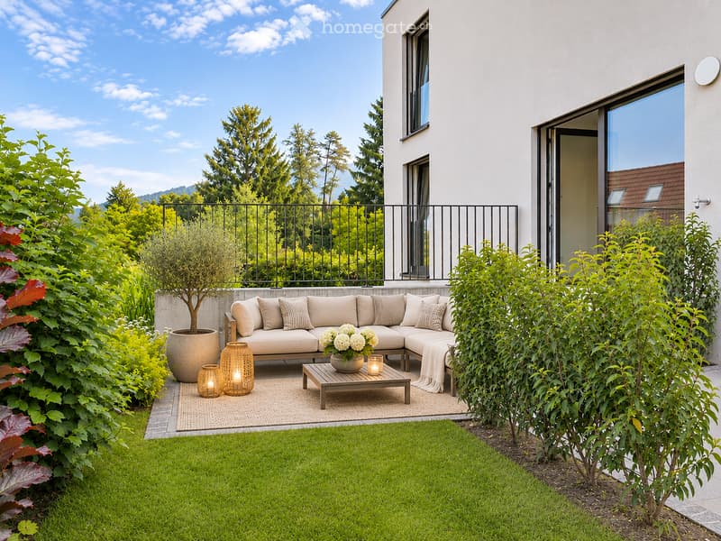 A modern outdoor seating area with a beige sectional sofa, coffee table, decorative candles, and a potted plant, surrounded by lush greenery and a well-maintained lawn.