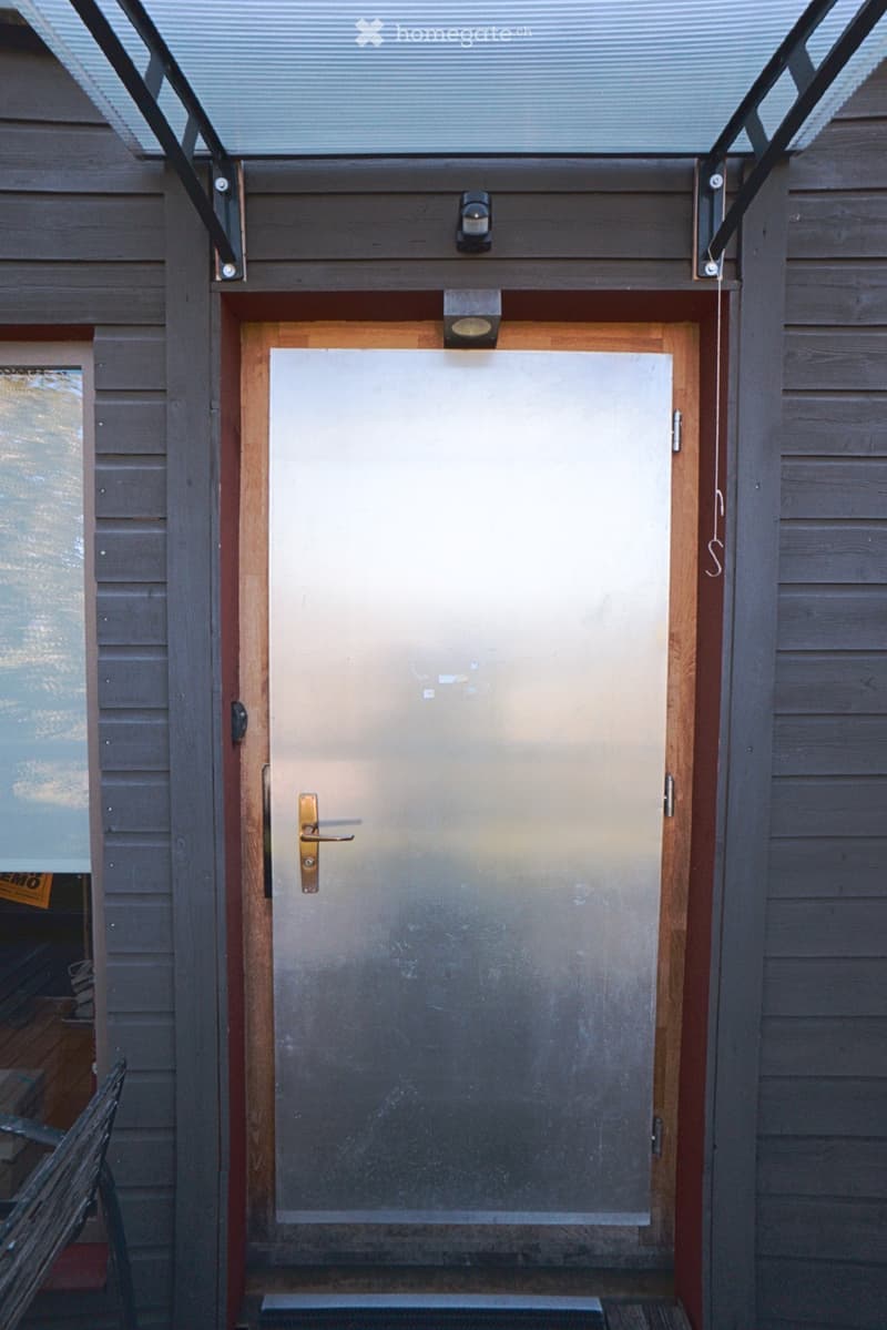 A closed garage door with a modern, sleek design, featuring a metallic finish and a brass handle, set within a wooden-framed structure with integrated lighting fixtures above.