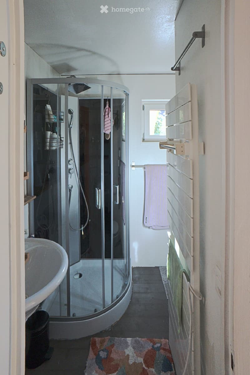 Modern bathroom with a bathtub, glass-enclosed shower, towel rack, and small window providing natural light.