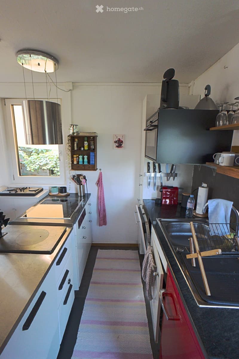 Modern kitchen with white cabinets, black countertops, and stainless steel appliances. Features include a refrigerator, microwave, oven, sink, and various kitchen utensils.