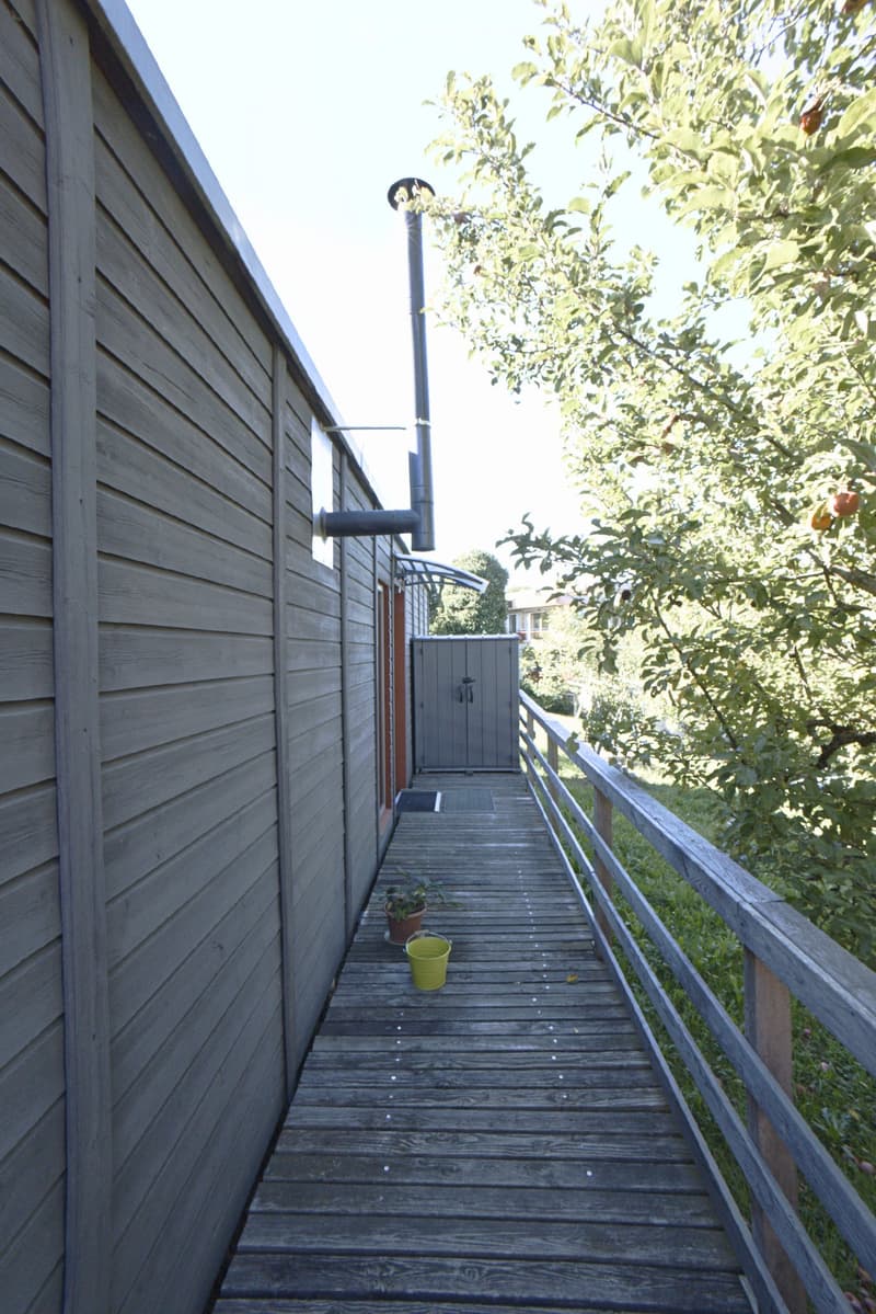 Wooden outdoor staircase leading up from a garden area, with a small storage shed and potted plants visible along the path.