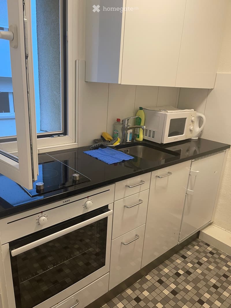 Modern kitchen with white cabinets, black countertops, stainless steel appliances, and a window with blinds.