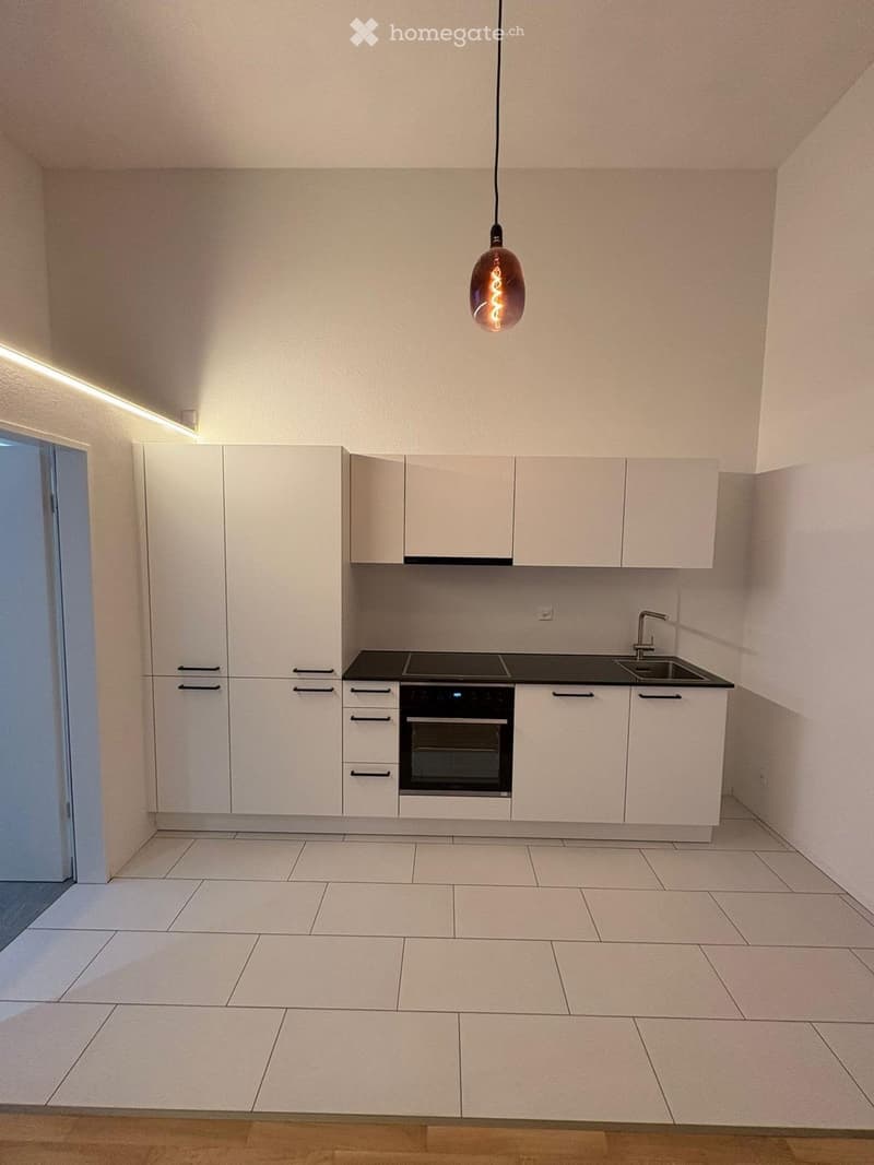 Modern kitchen with white cabinets, black countertop, built-in oven, sink, and pendant light fixture.