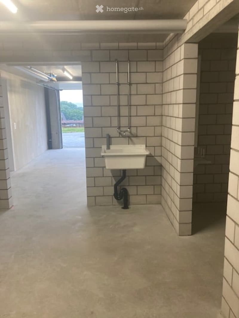 Empty utility or washroom area with a white sink, tiled walls, and concrete floor. No furniture or equipment present.