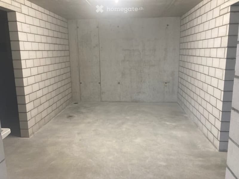 Empty room with concrete walls and floor, white tiled columns, and a single door.