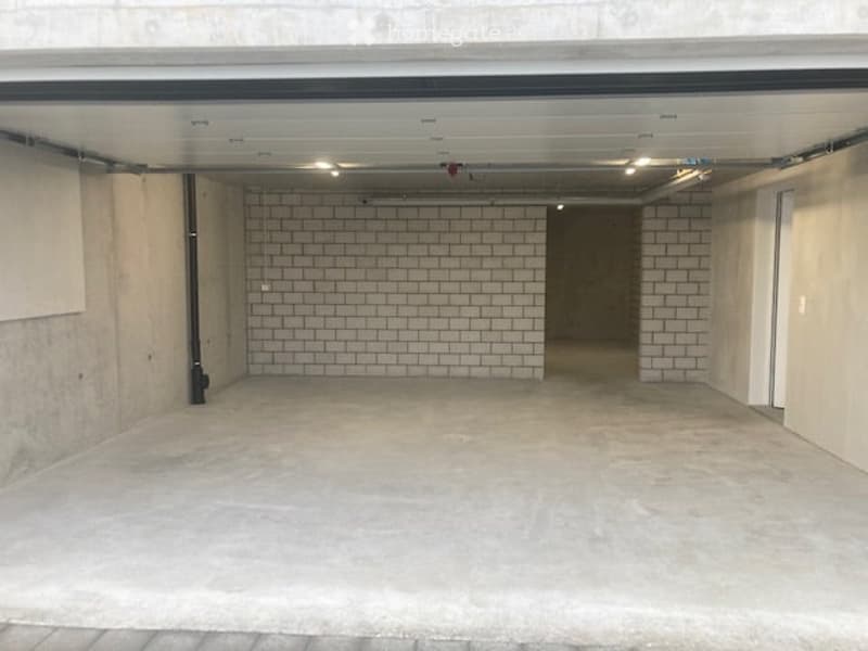 Empty garage with concrete floor, white brick walls, and overhead lighting.