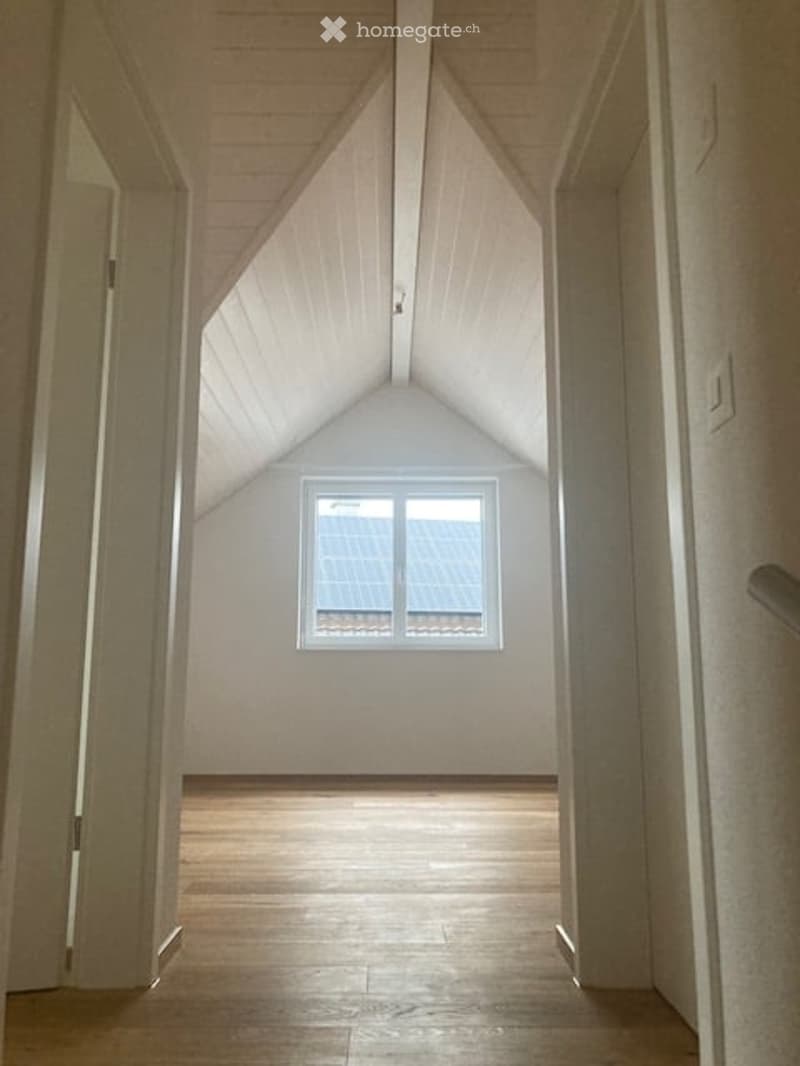 Empty room with wooden flooring, white walls, and a skylight window at the far end.