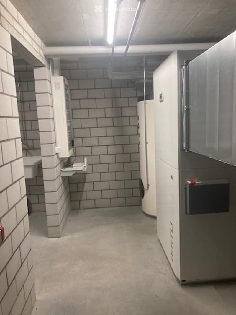 Utility room with white brick walls, concrete floor, water heater, and storage cabinets.