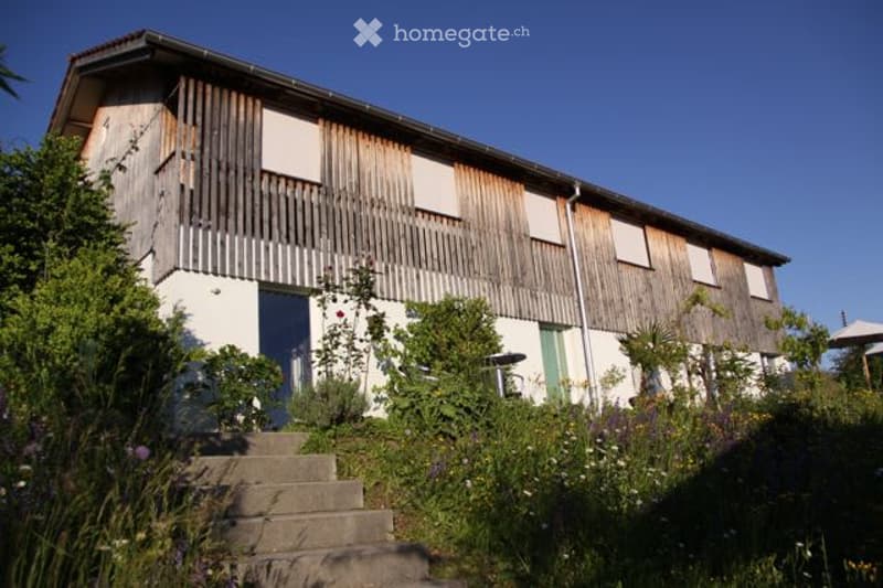 Two-story wooden house with white walls, raised ground floor, and steps leading up to the entrance.