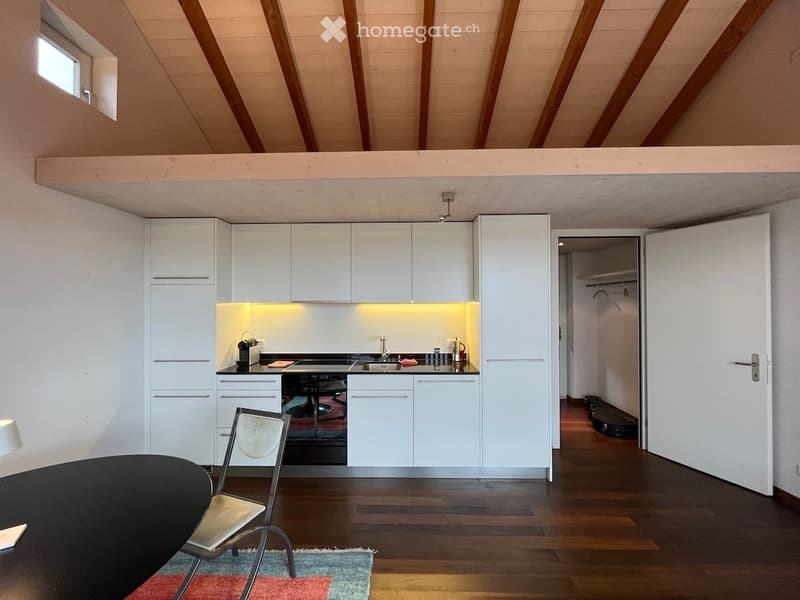 Modern kitchen with white cabinets, a sink, and a coffee maker. A black table and a chair are placed in the foreground, with a small rug on the floor.