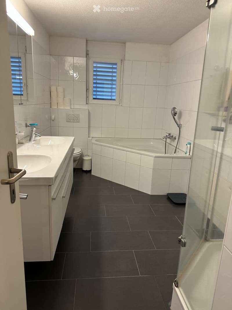 Modern bathroom with white tiles, black floor, double sink, bathtub, toilet, and shower area.