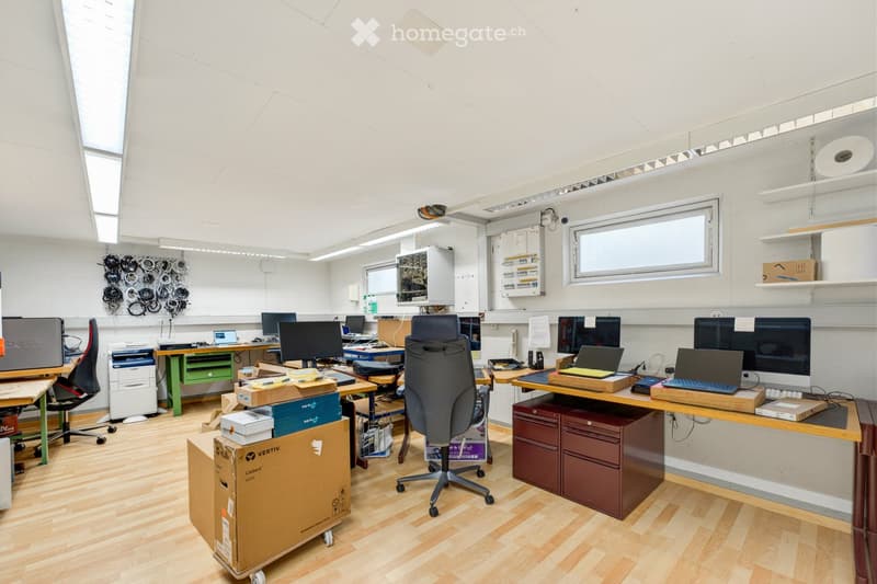 Office space with multiple desks, chairs, laptops, monitors, printers, and storage cabinets.