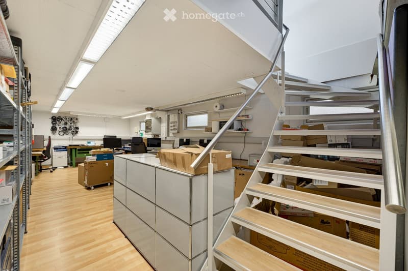 Office space with wooden flooring, large windows, desks, computers, and a staircase leading to an upper level.