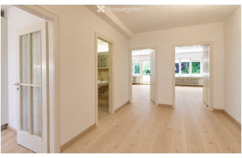 Empty hallway with light wooden flooring, white walls, and several open doors leading to other rooms.