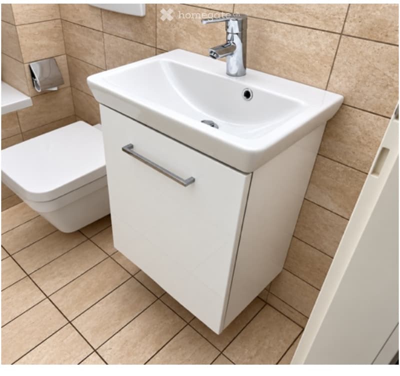 Modern bathroom with a white sink, chrome faucet, white cabinet, and toilet. Beige tiled walls and floor.