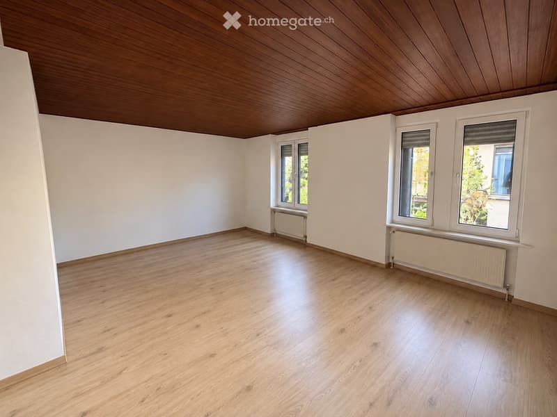 Empty room with light wooden flooring, white walls, and wooden ceiling. Three windows with white frames and radiators beneath them.