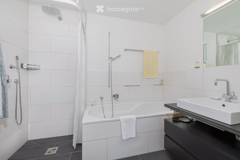 Modern bathroom with white tiles, bathtub, sink, mirror, and showerhead.