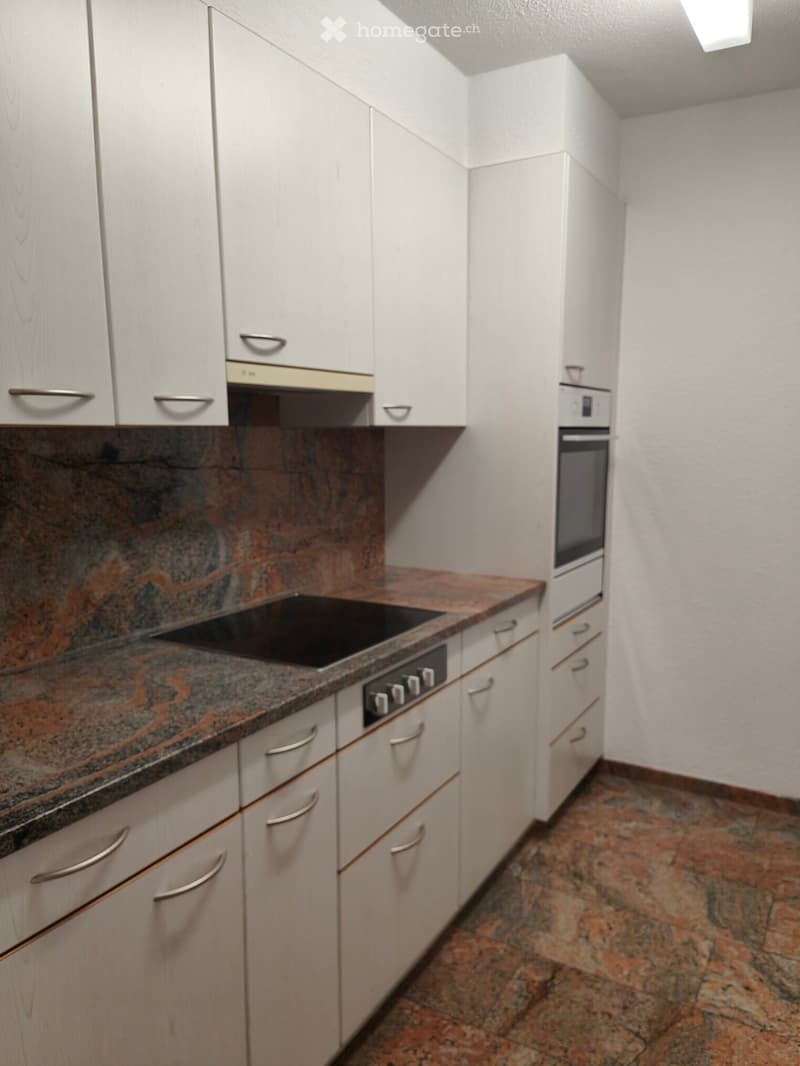 Modern kitchen with white cabinets, granite countertop, built-in stove, and oven. The floor is tiled with a stone pattern.