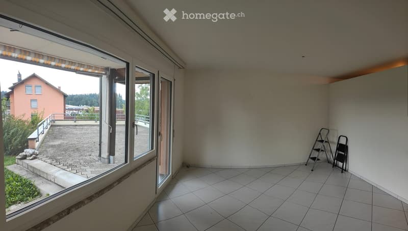 Empty room with tiled floor, large window with blinds, and two small ladders against the wall.