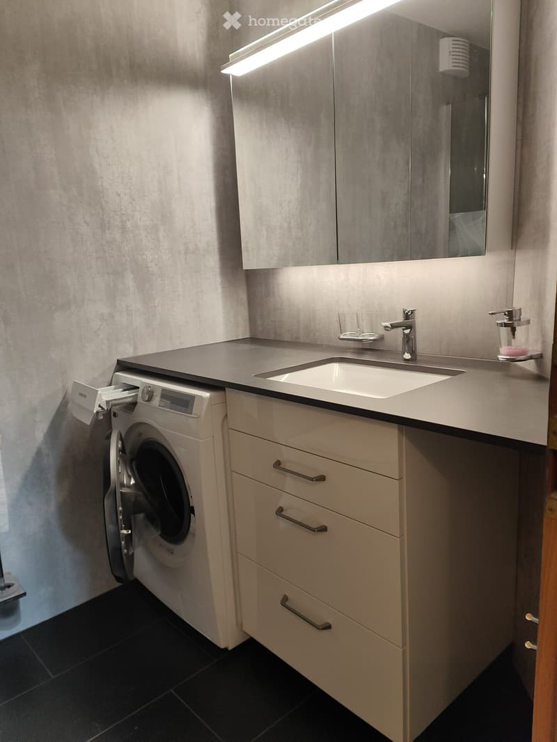 Modern bathroom with a sink, faucet, built-in washing machine, mirror, and storage cabinets.