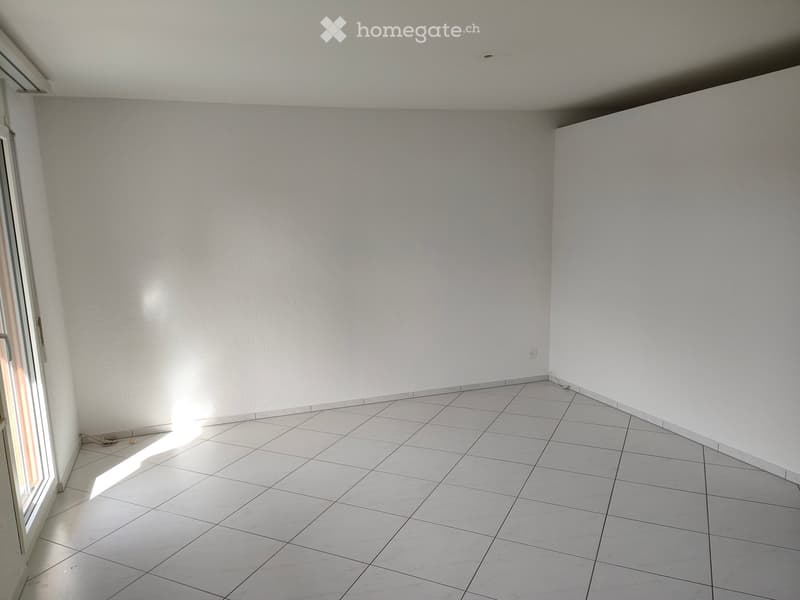 Empty room with white tiled floor and white walls, featuring a large window on one side allowing natural light to enter.