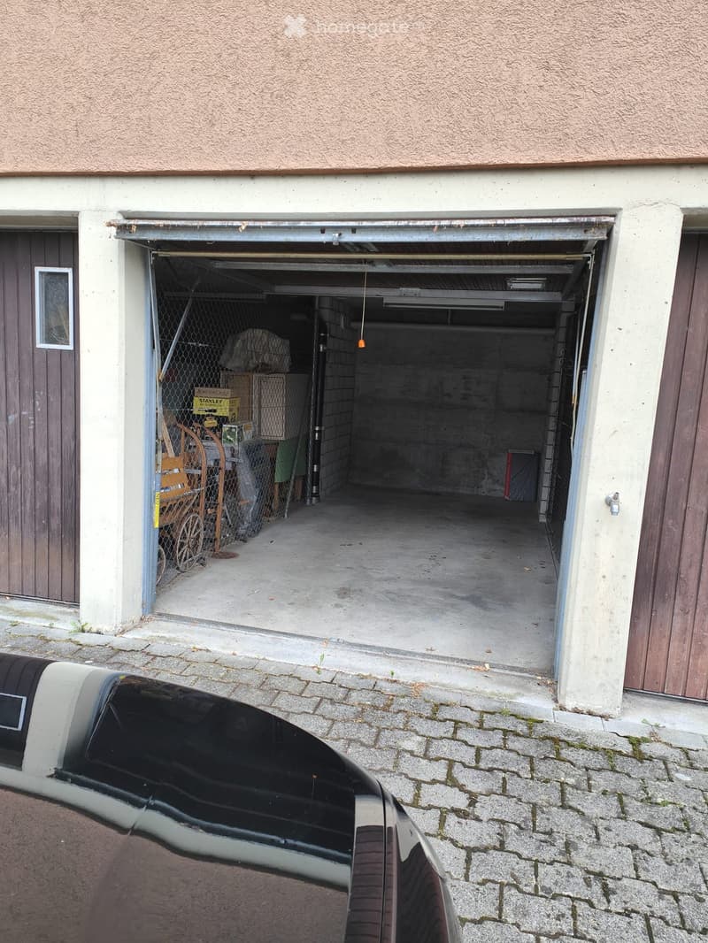 Open garage door showing storage items inside, with a car partially visible in the foreground.