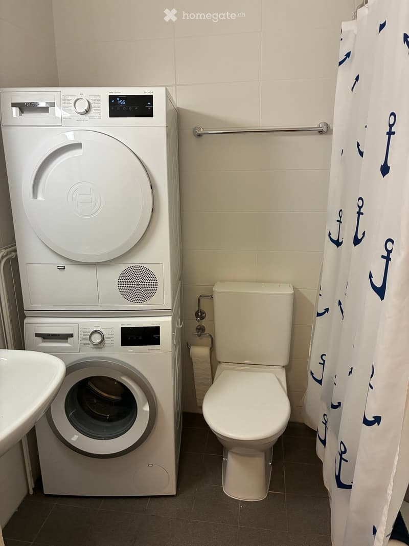 Bathroom with a white Bosch washing machine, toilet, and sink, with a shower curtain featuring anchor designs.