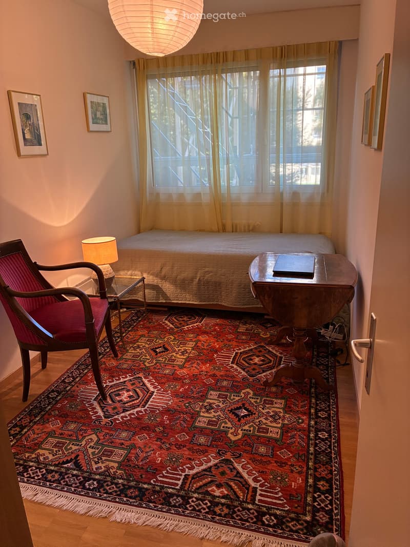 Cozy bedroom with a large bed, patterned rug, wooden chair, side table, and framed artwork on the walls.