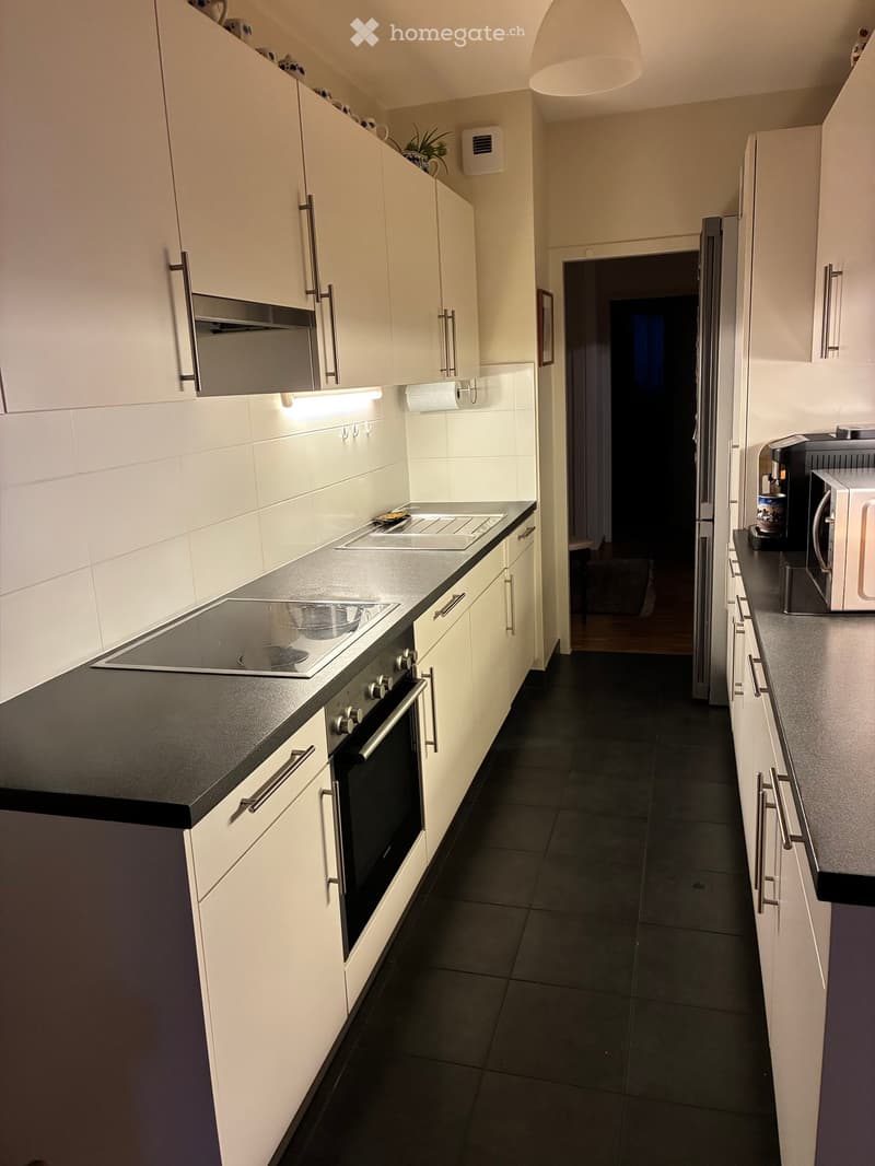 Modern kitchen with white cabinets, black countertops, stainless steel appliances, and dark tiled flooring.