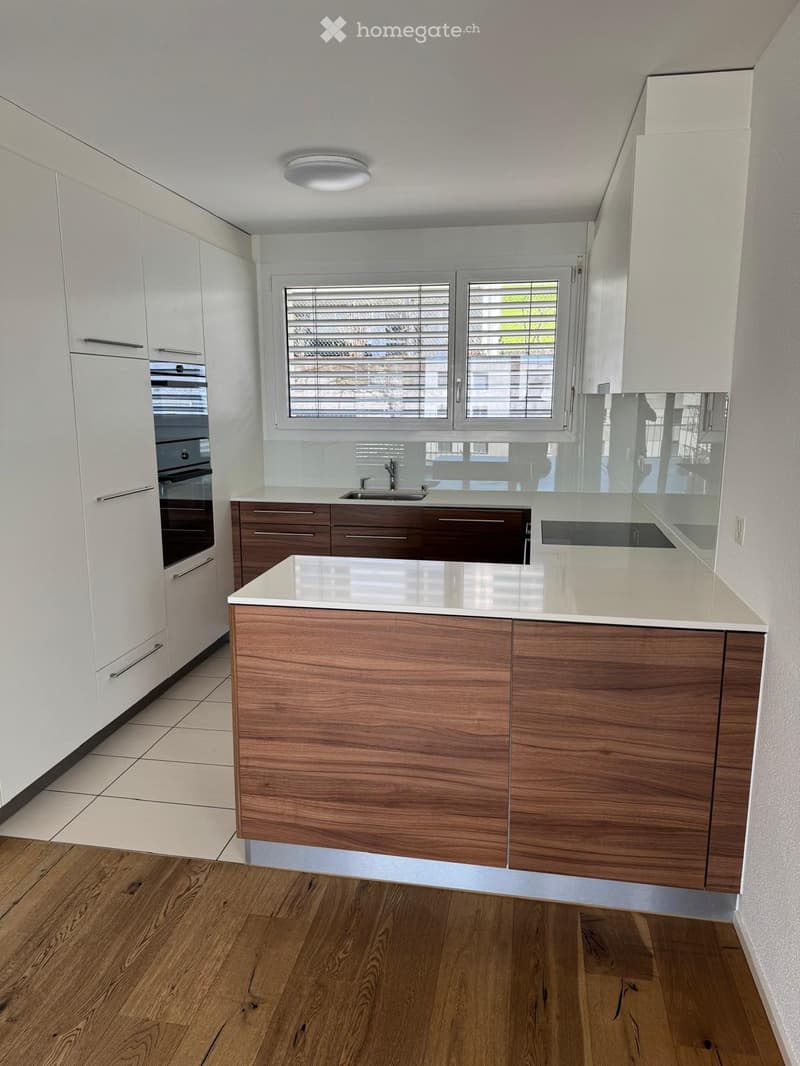 Modern kitchen with white and dark wood cabinets, a central island, and a sink. The space features a large window with blinds and a sleek, contemporary design.