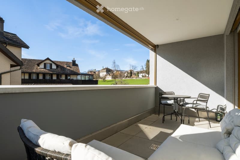 Balcony with a sofa, table, and chairs, overlooking a scenic town and green landscape.