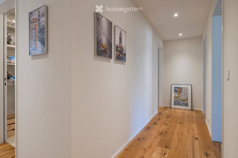 A narrow hallway with light wooden flooring, white walls, and several framed pictures, including one labeled 'DAVOS'.