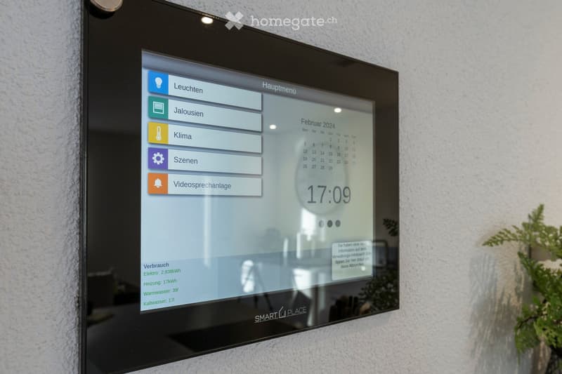 A wall-mounted smart home control panel displaying menu options, time, and energy consumption data.