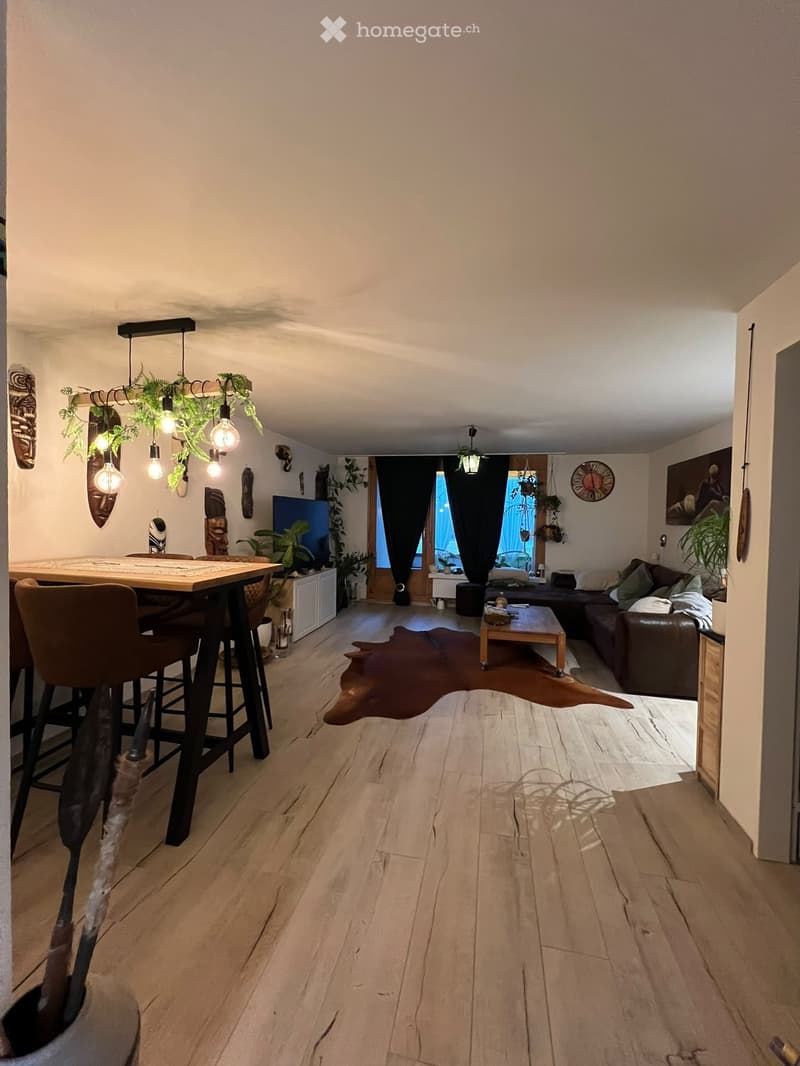 Modern living room with wooden flooring, a sofa, coffee table, dining table with chairs, and decorative plants.