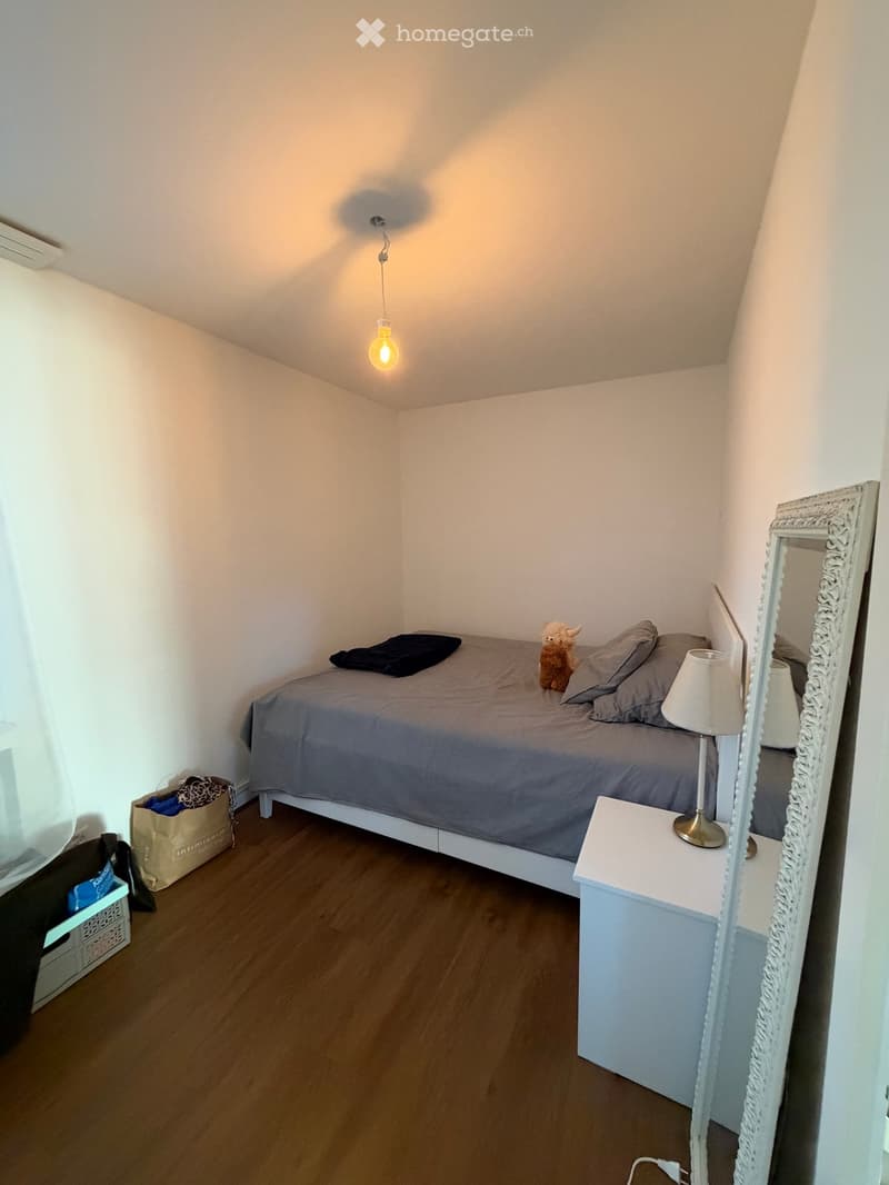 Cozy bedroom with a single bed, nightstand, lamp, mirror, and a small stuffed animal on the bed.