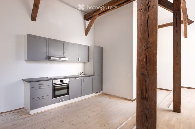Modern kitchen with grey cabinets, stainless steel appliances, and wooden flooring.