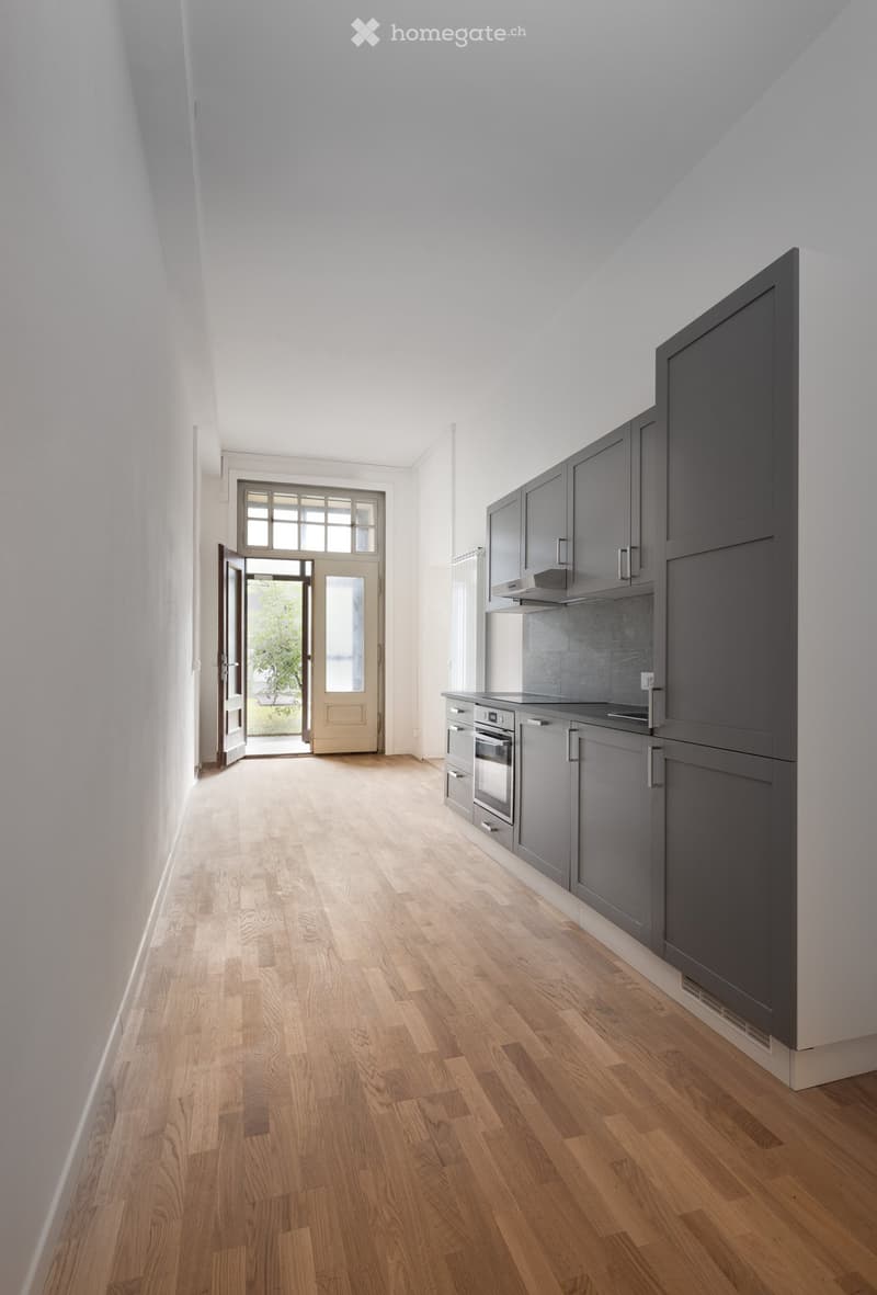 Empty room with light wooden flooring, grey cabinets, and a doorway leading outside.