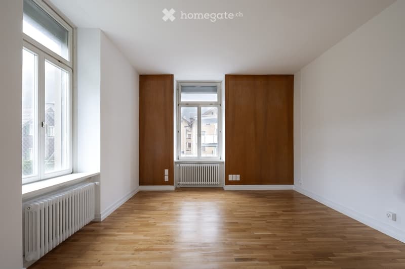 Empty room with wooden flooring, white walls, large windows, and radiators. No furniture or equipment present.