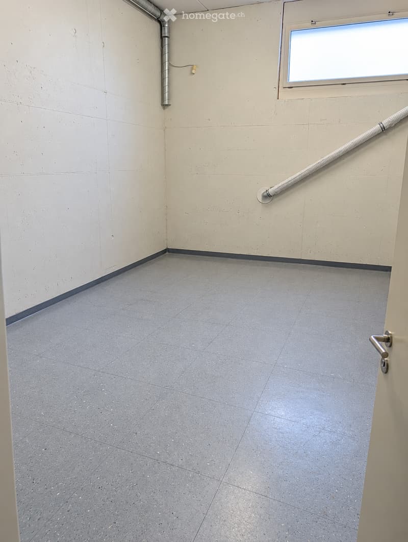 Empty room with grey tiled floor and light-colored walls, featuring a window, a door handle, and a small electrical outlet.