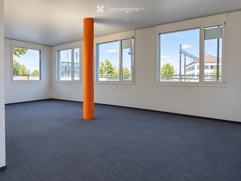 Empty room with white walls, blue carpet, large windows, and an orange column in the center.