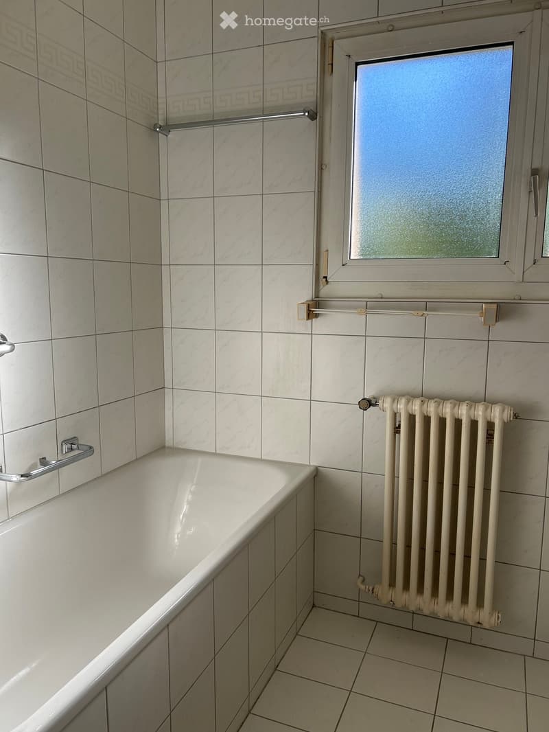 Bathroom with a white bathtub, tiled walls, a radiator, and a window with frosted glass.