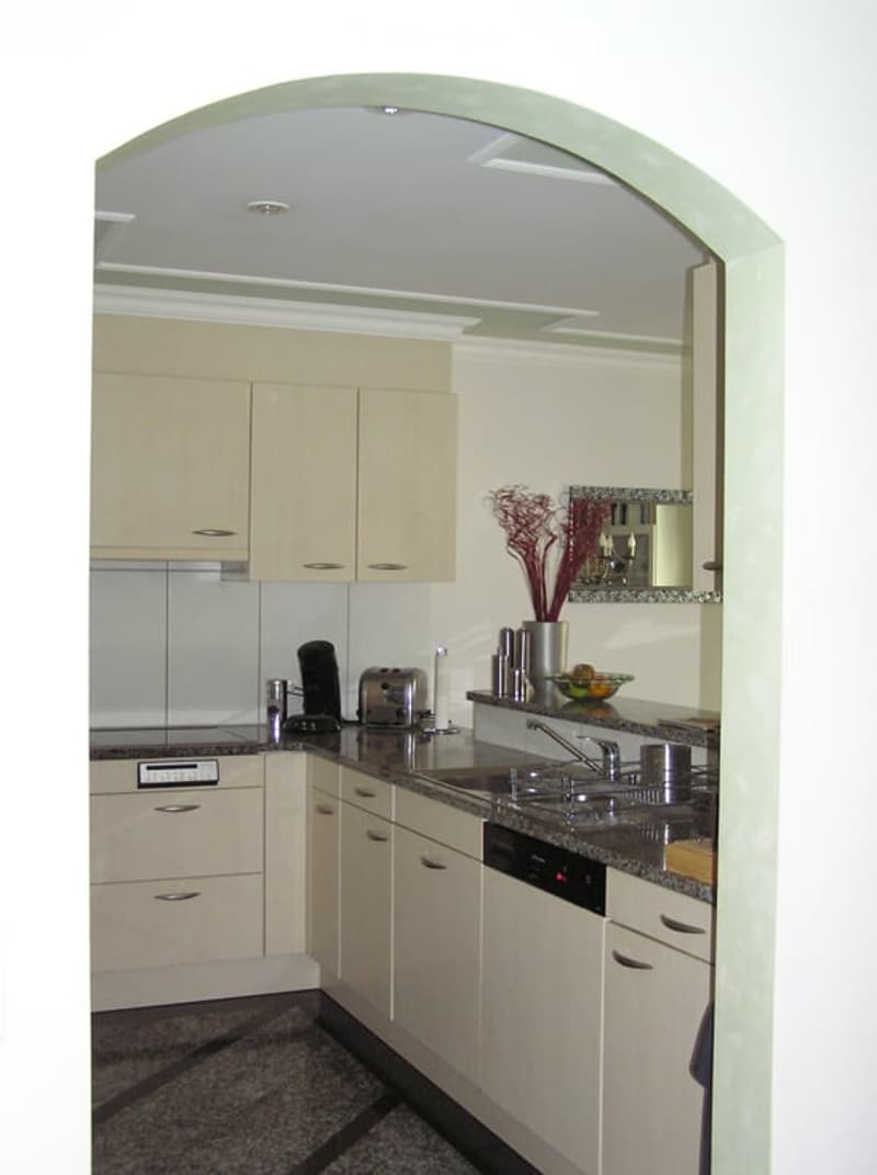 Modern kitchen with light-colored cabinets, stainless steel appliances, granite countertops, and a decorative vase on the counter.
