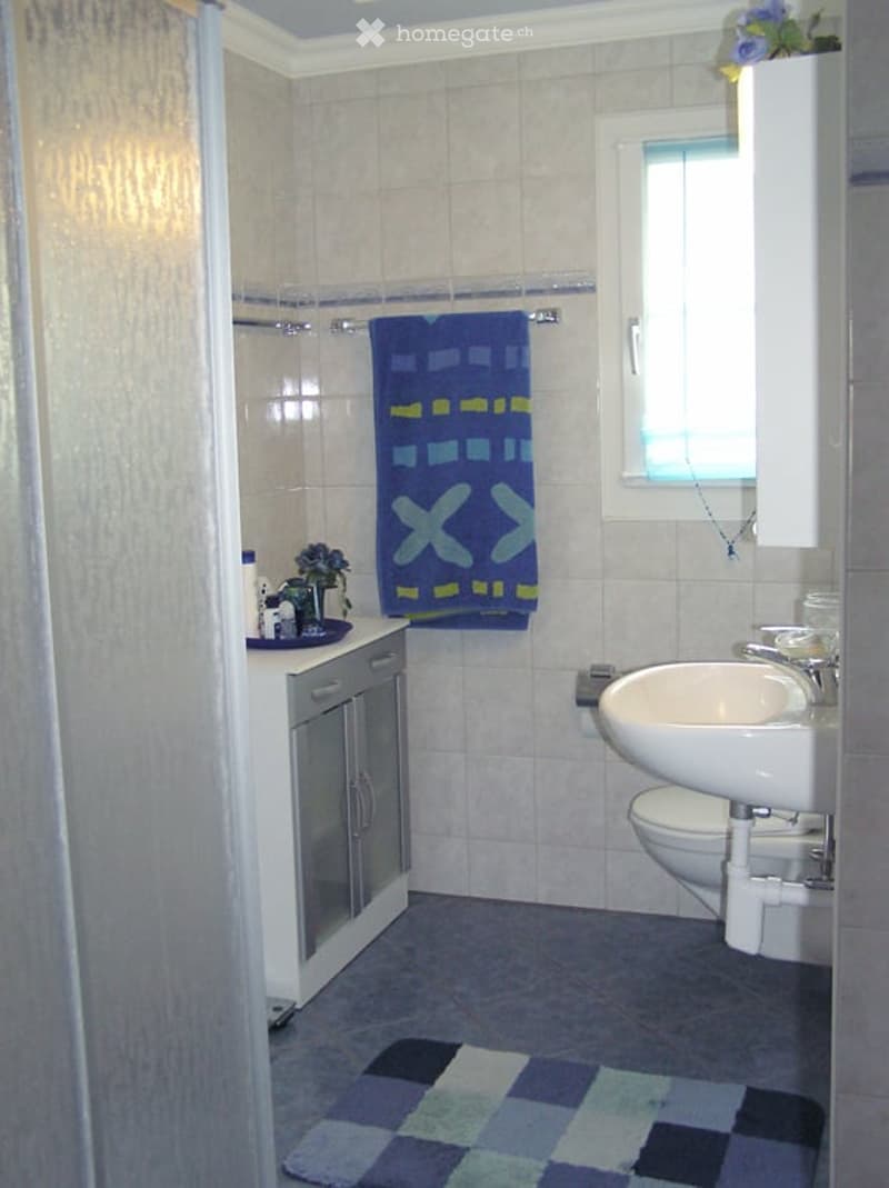 Bathroom with white tiles, a sink, toilet, cabinet, towel, and a small flower arrangement on the counter.