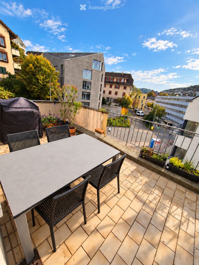Balcony with tiled floor, metal railing, table, chairs, and potted plants.