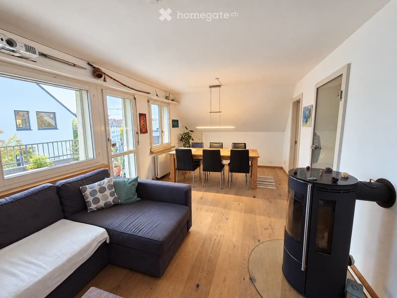 Modern living and dining area with wooden flooring, a grey sectional sofa with cushions, a coffee table, a dining table with chairs, and a modern fireplace.