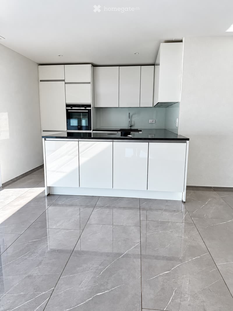 Modern kitchen with white cabinets, a black countertop, and a built-in oven. The floor is tiled with a marble-like pattern.