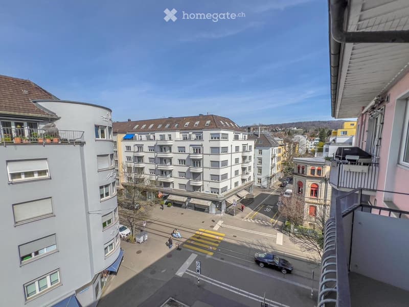 A balcony overlooking a city street with buildings, pedestrians, and traffic.